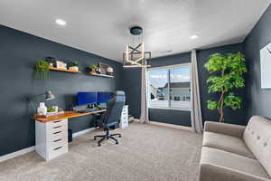 Carpeted office space featuring a textured ceiling and a notable chandelier