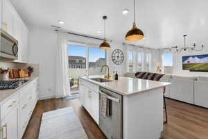 Kitchen featuring pendant lighting, white cabinetry, stainless steel appliances, sink, and a kitchen island with sink