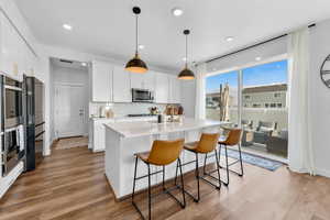 Kitchen with white cabinetry, hanging light fixtures, stainless steel appliances, and an island with sink