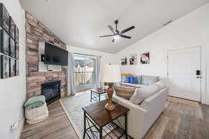 Living room with lofted ceiling, hardwood / wood-style floors, ceiling fan, and a stone fireplace