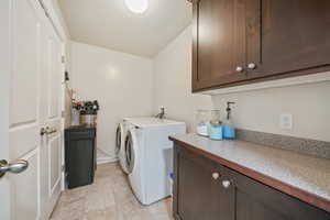 Clothes washing area featuring washer and dryer, cabinets, and a textured ceiling