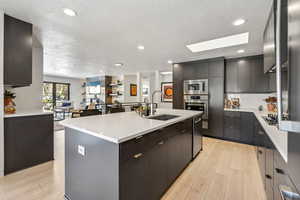 Kitchen with sink, a textured ceiling, stainless steel appliances, and an island with sink