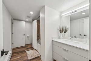 Bathroom featuring hardwood / wood-style flooring, a textured ceiling, vanity, and shower / bath combo