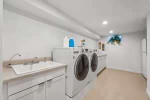 Clothes washing area with washer and dryer, sink, and cabinets