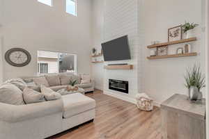 Living room with hardwood / wood-style flooring, a large fireplace, a towering ceiling, and a healthy amount of sunlight