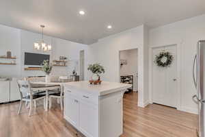 Kitchen featuring a center island, white cabinetry, hanging light fixtures, light wood-type flooring, and stainless steel fridge