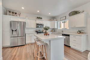 Kitchen featuring a center island, white cabinetry, light wood-type flooring, sink, and stainless steel appliances