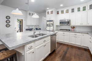 Kitchen featuring an island with sink, appliances with stainless steel finishes, pendant lighting, white cabinets, and sink