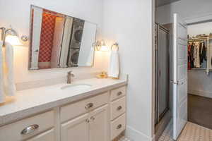 Bathroom featuring stacked washer / dryer, walk in shower, vanity, and tile patterned flooring