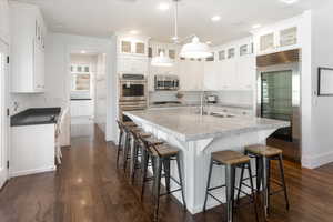 Kitchen with decorative light fixtures, a kitchen island with sink, appliances with stainless steel finishes, dark wood flooring, and white cabinets