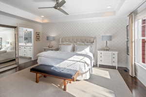 Bedroom with ceiling fan, connected bathroom, dark hardwood / wood-style floors, and a tray ceiling