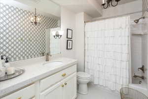 Full bathroom with toilet, vanity, an inviting chandelier, and shower / bath combination with curtain