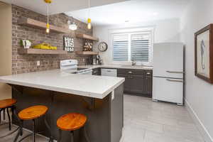 Kitchen featuring kitchen peninsula, white appliances, pendant lighting, a breakfast bar, and sink