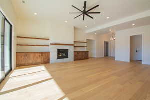 Unfurnished living room featuring ceiling fan with notable chandelier, light hardwood / wood-style flooring, and a high end fireplace