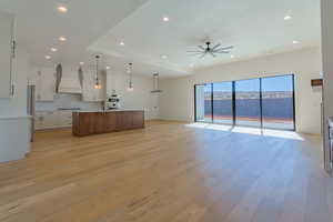 Kitchen with light hardwood / wood-style flooring, a spacious island, custom range hood, decorative light fixtures, and white cabinetry