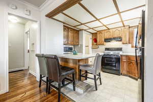 Kitchen with black refrigerator, crown molding, gas range oven, a kitchen breakfast bar, and light hardwood / wood-style flooring