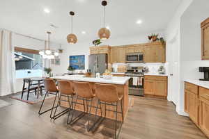 Kitchen with decorative light fixtures, hardwood / wood-style floors, a breakfast bar, a kitchen island with sink, and stainless steel appliances