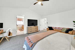 Bedroom with ensuite bathroom, light colored carpet, ceiling fan, and vaulted ceiling