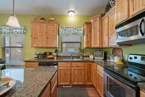 Kitchen with dark tile patterned flooring, appliances with stainless steel finishes, a textured ceiling, decorative light fixtures, and sink