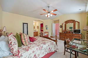 Carpeted bedroom featuring lofted ceiling, ensuite bath, and ceiling fan