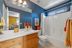 Full bathroom featuring toilet, a textured ceiling, tile patterned flooring, shower / bath combination with curtain, and vanity