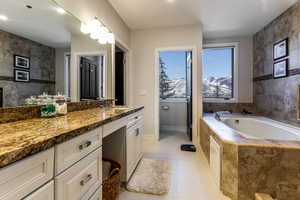 Bathroom featuring tile patterned floors, tile walls, a mountain view, a relaxing tiled tub, and vanity