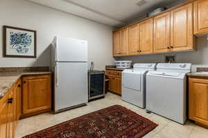 Washroom with washer and dryer, light tile patterned floors, beverage cooler, and cabinets