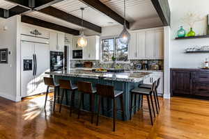 Kitchen with black appliances, white cabinetry, dark stone countertops, a kitchen island, and pendant lighting