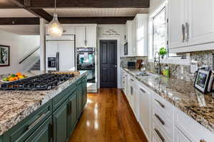 Kitchen with white cabinets, built in appliances, sink, green cabinetry, and beam ceiling