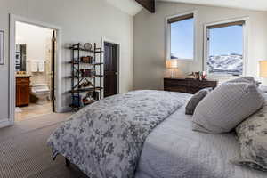 Carpeted bedroom featuring a mountain view, vaulted ceiling with beams, and ensuite bathroom