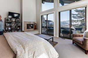 Carpeted bedroom with a tile fireplace, a mountain view, a towering ceiling, and access to outside