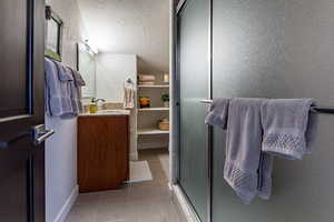 Bathroom with vanity, a shower with shower door, a textured ceiling, and tile patterned flooring