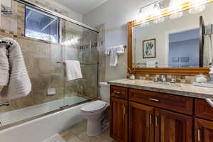 Full bathroom featuring bath / shower combo with glass door, toilet, vanity, and tile patterned flooring