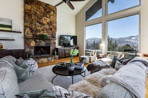 Living room featuring hardwood / wood-style floors, a healthy amount of sunlight, high vaulted ceiling, and a stone fireplace