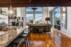 Kitchen featuring a stone fireplace, hardwood / wood-style flooring, pendant lighting, light stone counters, and a breakfast bar area