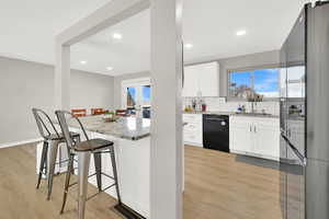 Kitchen with light stone countertops, sink, black dishwasher, and white cabinetry