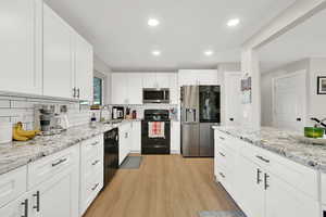 Kitchen featuring backsplash, black appliances, sink, white cabinetry, and light hardwood / wood-style flooring