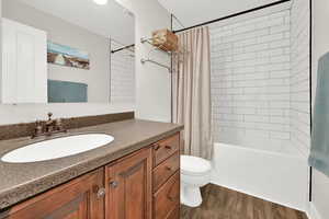 Full bathroom with toilet, vanity, shower / tub combo with curtain, and hardwood / wood-style flooring