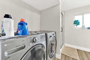 Clothes washing area with light wood-type flooring and independent washer and dryer