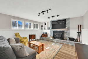 Living room featuring rail lighting, a fireplace, wood-type flooring, and built in shelves