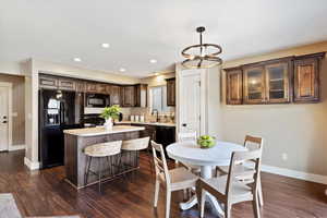 Kitchen with pendant lighting, dark wood-type flooring, a center island, black appliances, and dark brown cabinetry