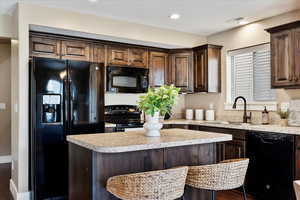 Kitchen featuring sink, hardwood / wood-style floors, black appliances, and a breakfast bar area