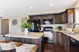 Kitchen featuring dark wood-type flooring, sink, black appliances, and a center island