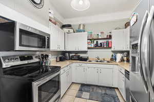 Kitchen featuring sink, white cabinetry, light tile patterned floors, and stainless steel appliances MAIN HOME