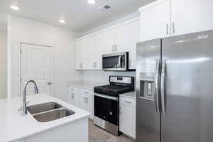 Kitchen with white cabinets, appliances with stainless steel finishes, sink, light wood-type flooring, and light stone counters