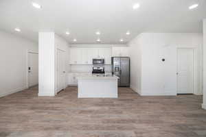 Kitchen with white cabinetry, stainless steel appliances, an island with sink, sink, and light hardwood / wood-style flooring