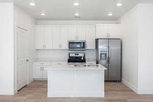 Kitchen with appliances with stainless steel finishes, a kitchen island with sink, white cabinets, light wood-type flooring, and sink