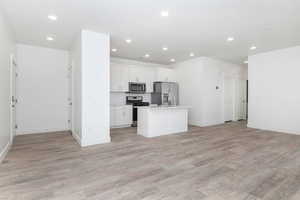 Kitchen with white cabinetry, light hardwood / wood-style flooring, stainless steel appliances, and a kitchen island with sink