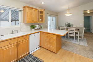 Kitchen with dishwasher, sink, kitchen peninsula, pendant lighting, and vaulted ceiling