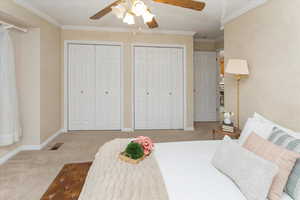 Carpeted bedroom featuring ceiling fan, two closets, and ornamental molding